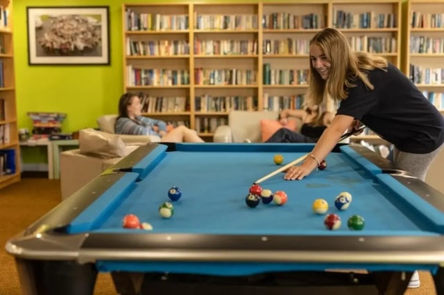 Students play pool in lounge with bookshelves living room at Bonington Student Village in Loughborough Student Accommodation