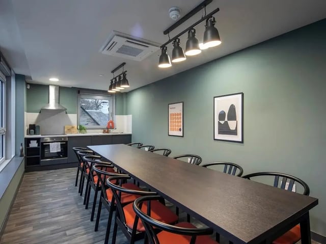 Long table with orange chairs and kitchen area common room at Norton's Student Living in Edinburgh Student Accommodation