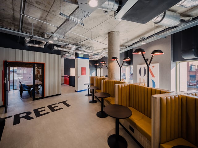 Yellow booths with tables and industrial ceiling lounge area at Vita Student Bruce Street in Belfast Student Accommodation