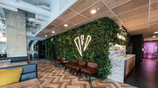 Green wall neon logo leather chairs and kitchen area at Vita Student Lewisham Exchange in London Student Accommodation