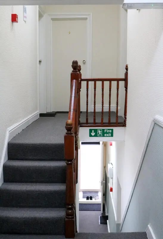 Carpeted stairs wooden railing fire exit sign hallway interior at 42 Disraeli Rd E7 9JP in London Student Accommodation