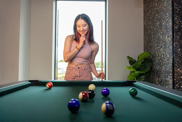 Woman with pool cue near billiards table playing area at Fusion Students Brent Cross in London Student Accommodation