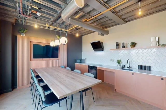 Large table with chairs and kitchen area. at Bridgeside in Nottingham Student Accommodation
