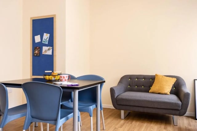 Table chairs bulletin board grey sofa living room at Bournemouth University Village - Chesil House in Bournemouth Student Accommodation