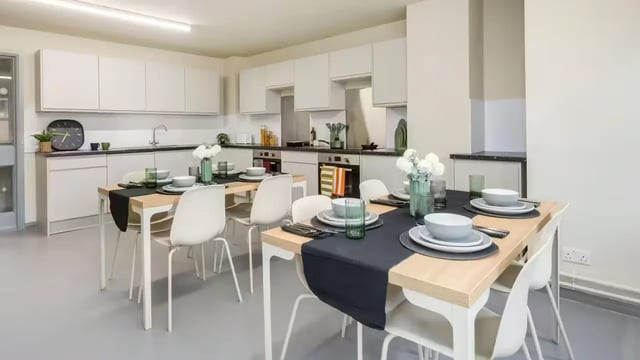 Dining tables with place settings and kitchen area at Hardwick Campus in Cheltenham Student Accommodation