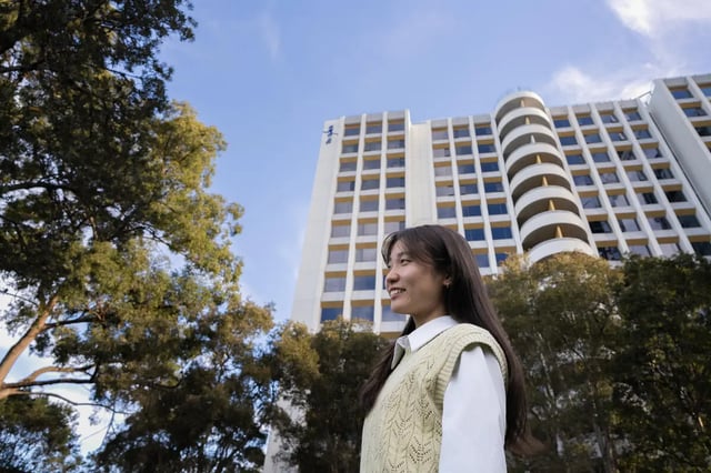 Student in front of tall building exterior at The Switch Lachlan Macquarie Park in Sydney Student Accommodation
