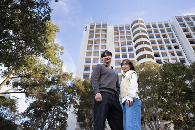 Students stand before a white building exterior at The Switch Lachlan Macquarie Park in Sydney Student Accommodation