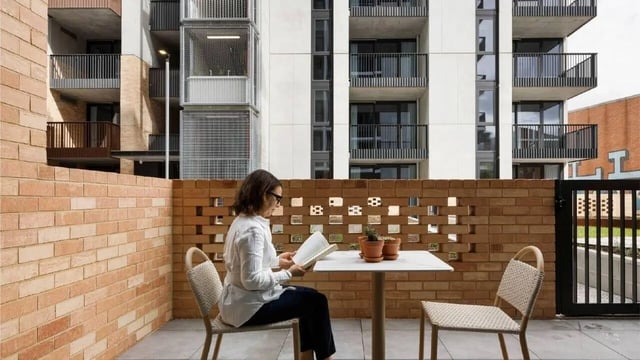 Woman reading at a table chairs exterior at Assemble Swiftwalk in Melbourne Student Accommodation