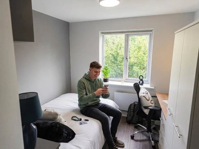 Man on bed with phone study desk wardrobe bedroom at City Edge - Manchester in Manchester Student Accommodation