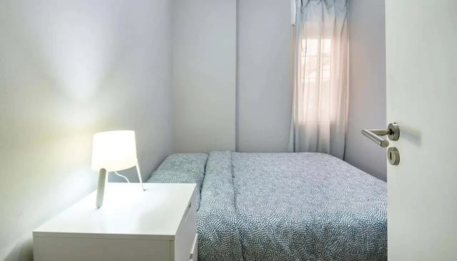 Bed with patterned duvet and bedside lamp bedroom at Casa Abel II – Room 5 in Lisbon Student Accommodation