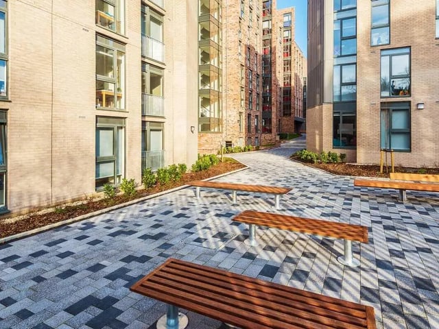 Wooden benches on patterned courtyard outside buildings exterior at Dunaskin Mill in Glasgow Student Accommodation
