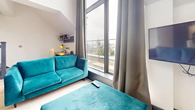 Teal sofa ottoman desk with lamp and TV living room at The Residence in Coventry Student Accommodation
