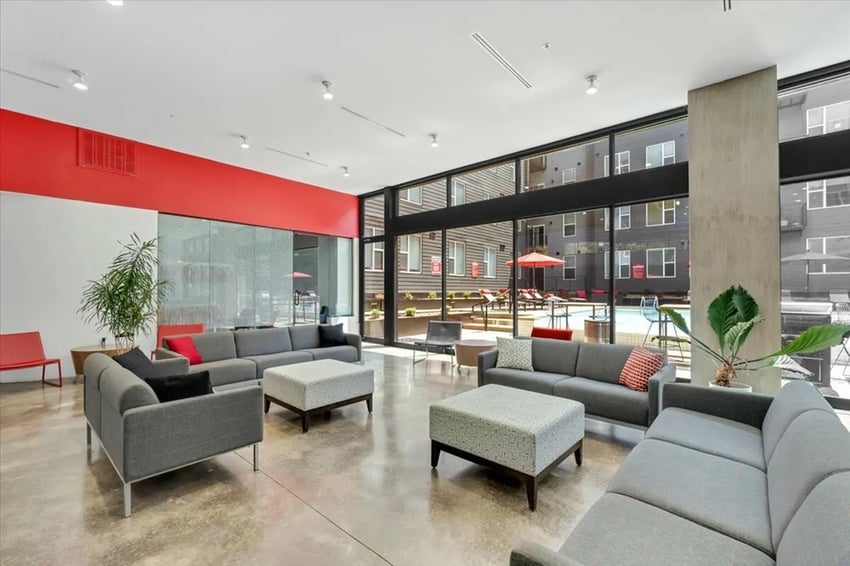 Grey sectional sofas with ottomans and plants living room at The Cardinal at West Center in Fayetteville Student Accommodation