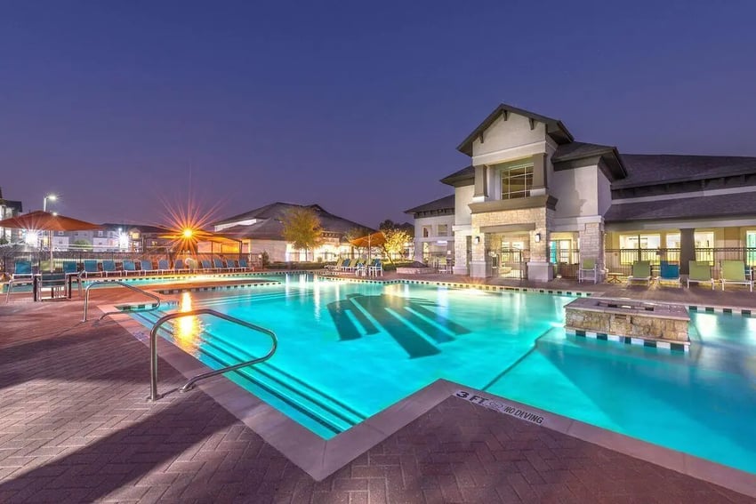 Illuminated swimming pool with lounge chairs and building exterior. at Forum at Denton Station in Denton Student Accommodation