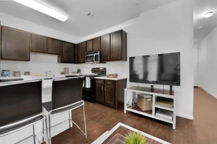Dark cabinets kitchen island two bar stools TV living room at GrandMarc Austin in Austin Student Accommodation