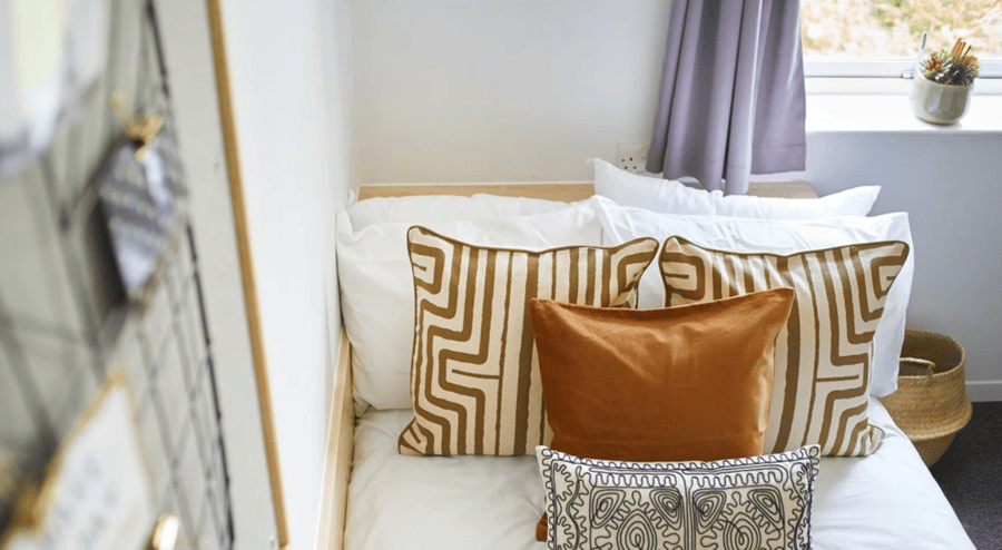 Bed with patterned cushions and laundry basket Bedroom at The Green in Bradford Student Accommodation
