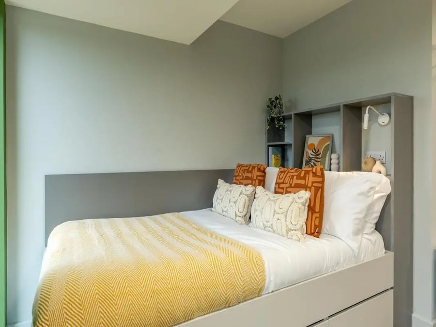 Bed with pillows shelves and plant bedroom at Venue Studios in London Student Accommodation