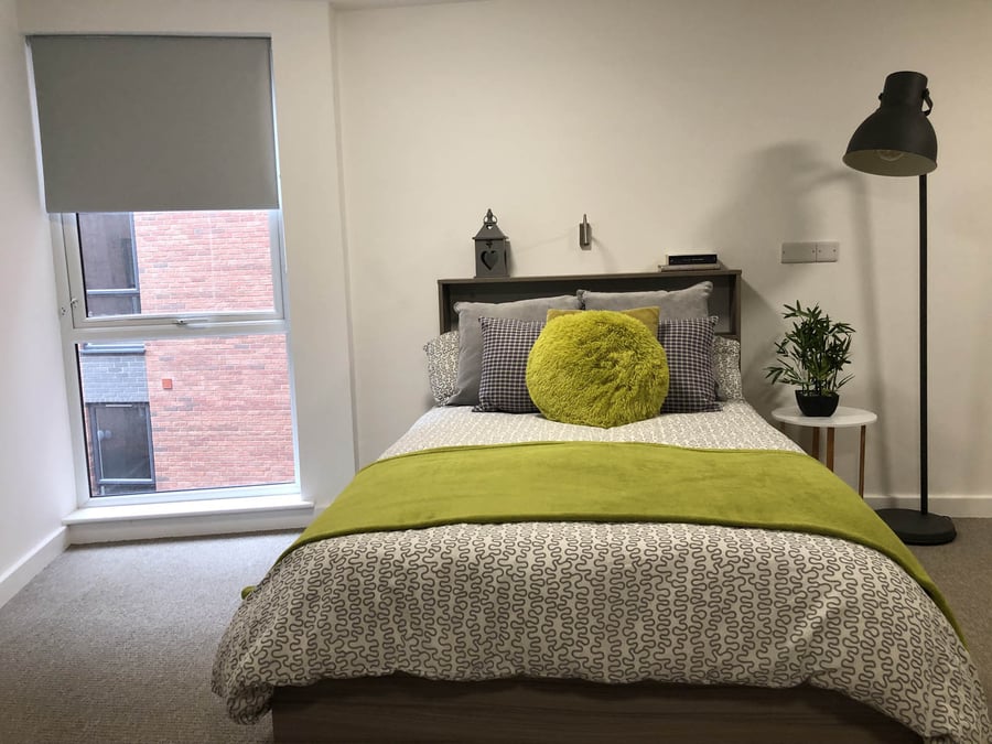 Bed with green throws pillows and window bedroom at Q Studios in Stoke-On-Trent Student Accommodation