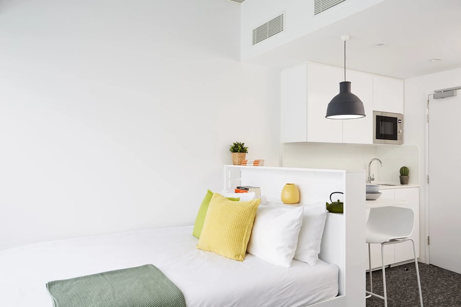 Bed with pillows and kitchen area bedroom at Scape Carlton in Melbourne Student Accommodation