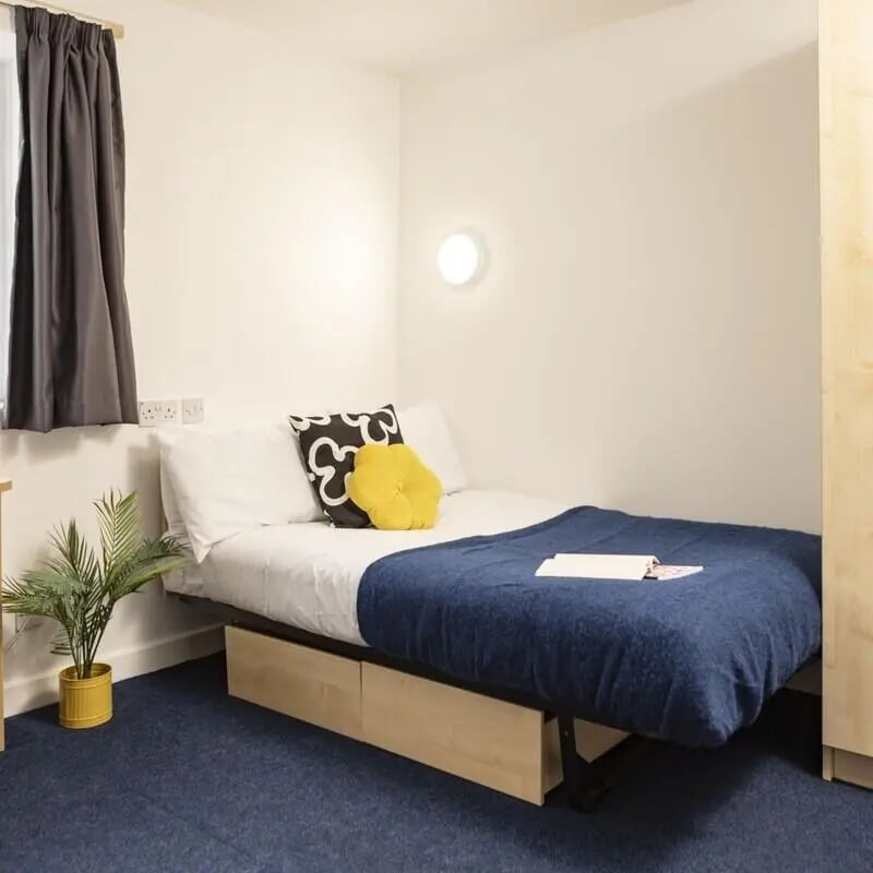 Bed with blue blanket yellow pillow study area at Albert Court in Liverpool Student Accommodation