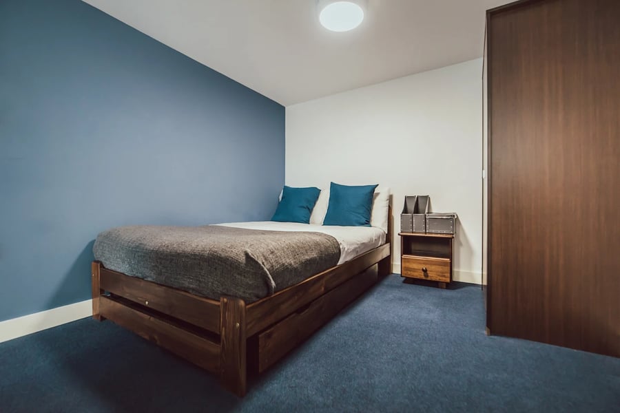 Wooden bed two blue pillows bedside table bedroom at Lomax Halls in Stoke-On-Trent Student Accommodation
