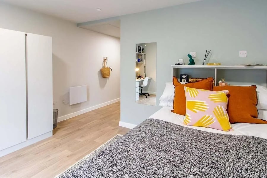 Bed with orange and pink pillows and storage bedroom at The Refinery in Leeds Student Accommodation