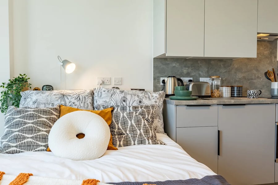 Bed with patterned pillows and kitchenette studio kitchen at Winfield Court in Nottingham Student Accommodation