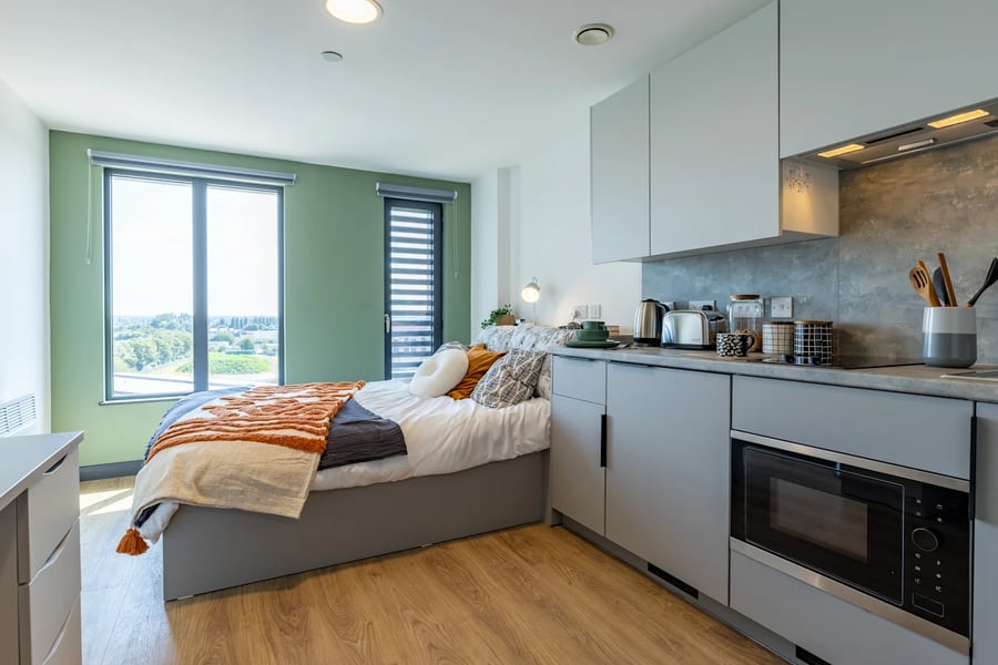 Bed with orange throw kitchen area microwave bedroom at Winfield Court in Nottingham Student Accommodation