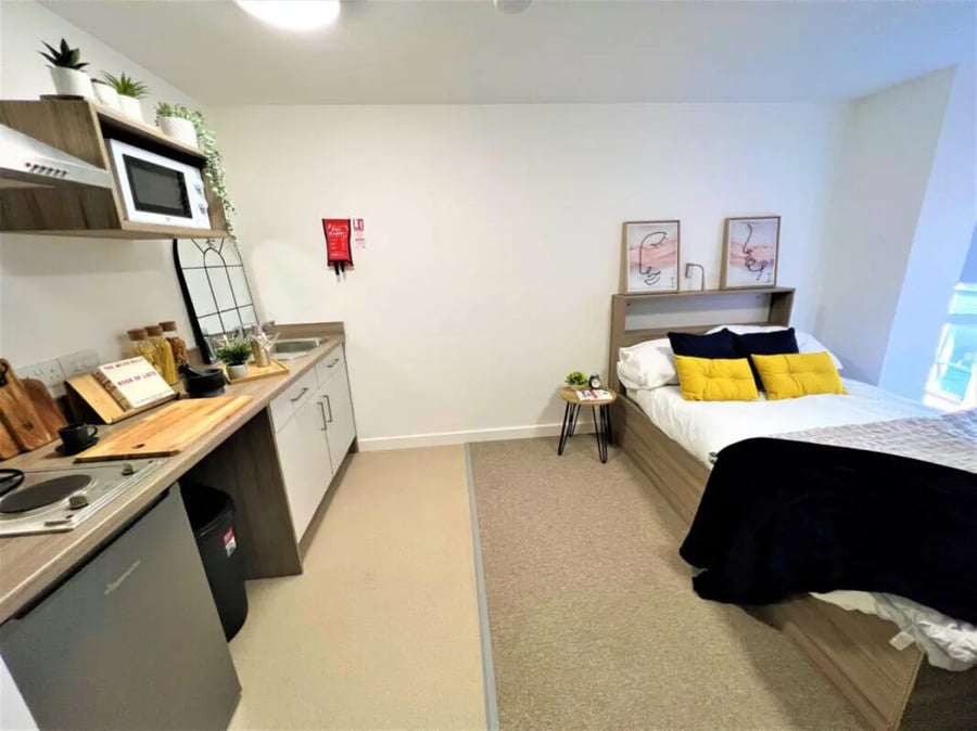 Kitchenette and bed with yellow pillows Bedroom at Q Studios in Stoke-On-Trent Student Accommodation