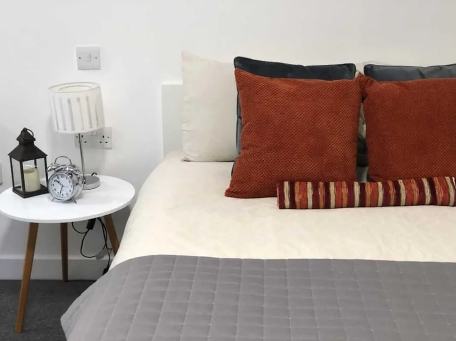 Bed with orange pillows alarm lamp and side table bedroom at Tudor Studios in Leicester Student Accommodation