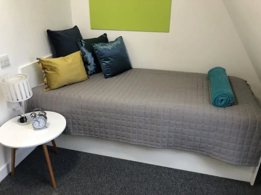 Bed with pillows clock lamp small table bedroom at Tudor Studios in Leicester Student Accommodation