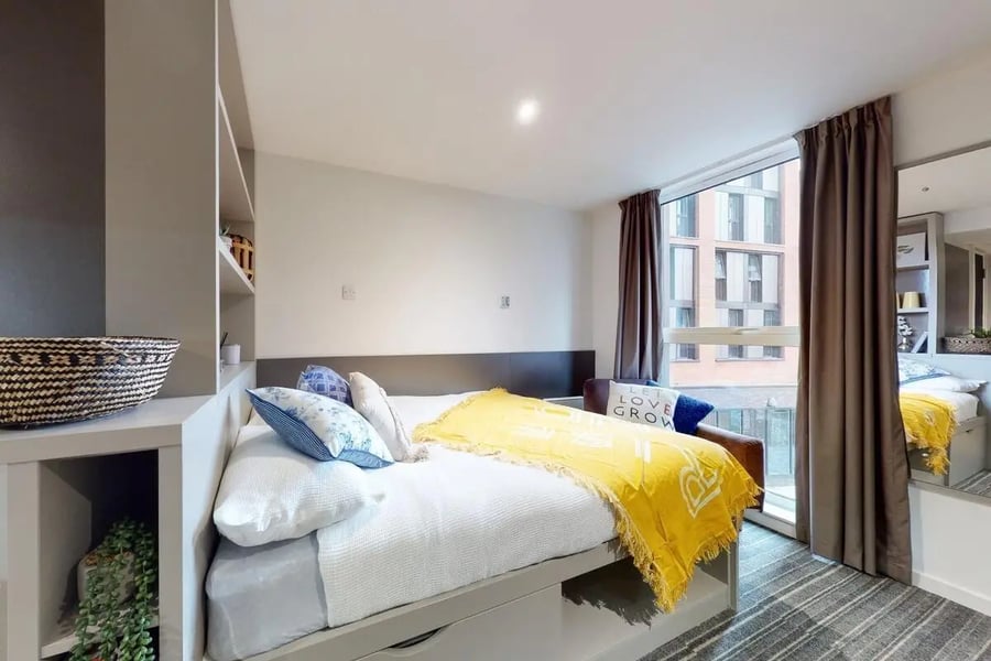 Bed with yellow blanket shelves baskets bedroom at Canvas Coventry City Point in Coventry Student Accommodation