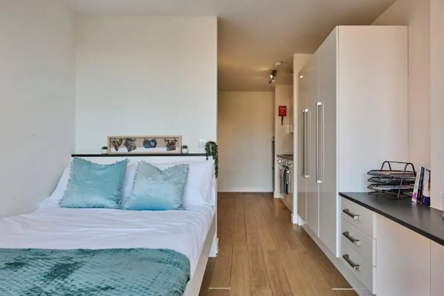 Bed with blue pillows and kitchen area studio apartment at The Summit Leicester in Leicester Student Accommodation