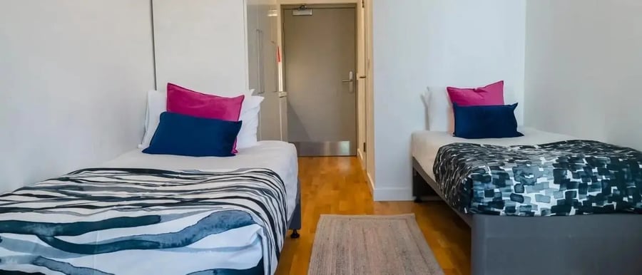 Two beds with colorful pillows and patterned duvet bedroom at Chapter Kings Cross in London Student Accommodation