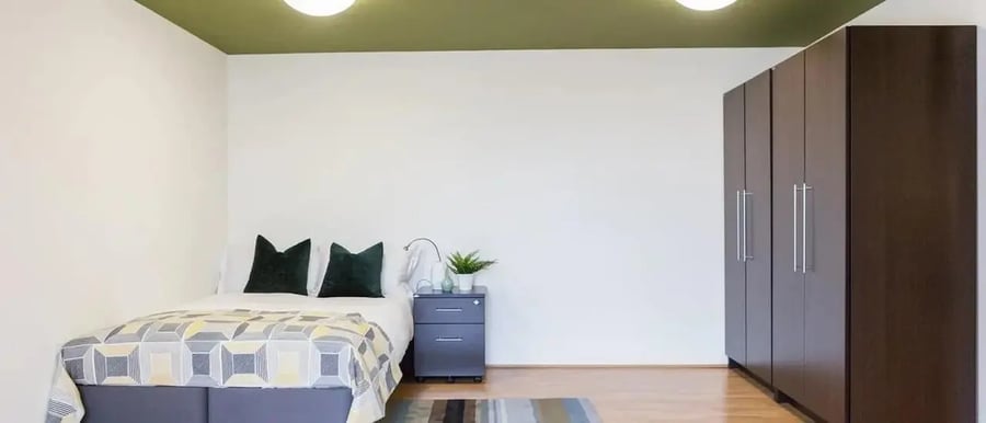 Bed with dark pillows and tall dark wardrobe bedroom at Chapter Spitalfields in London Student Accommodation
