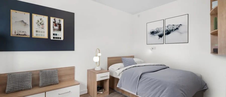 Bed with grey bedding desk lamp bench and artwork bedroom at Chapter Highbury in London Student Accommodation