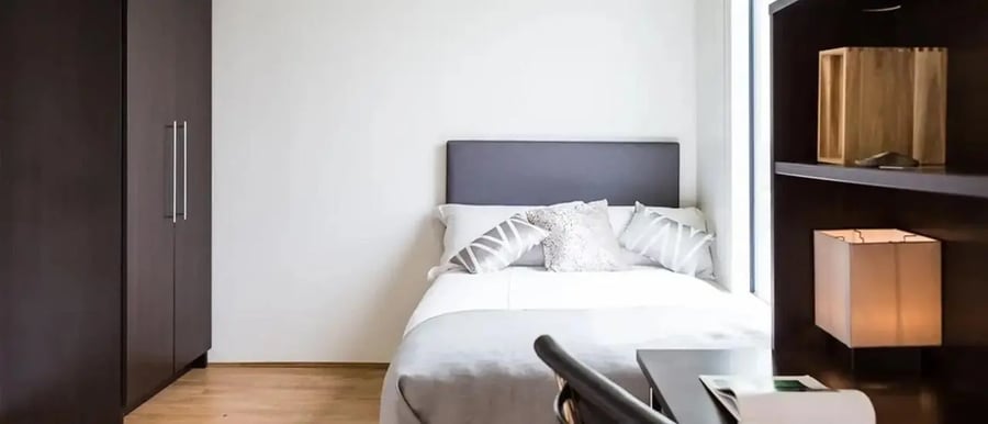 Dark wardrobe bed with pillows shelving unit bedroom at Chapter Portobello in London Student Accommodation