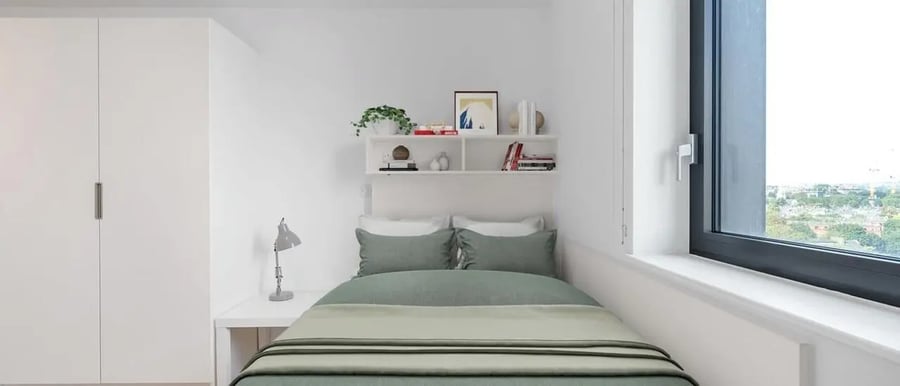 Bed with green bedding white wardrobe shelves bedroom at Chapter Highbury II in London Student Accommodation