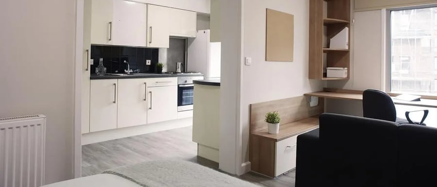 Kitchen cabinets radiator desk chair and couch living area at Chapter South Bank in London Student Accommodation