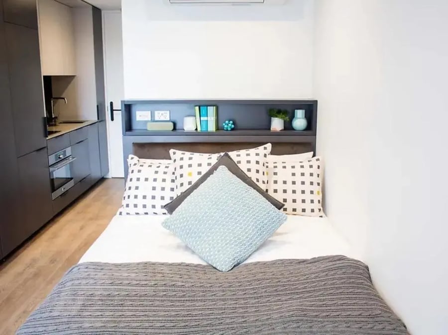 Bed with patterned pillows and kitchen area Bedroom at Yugo University Square Melbourne in Melbourne Student Accommodation