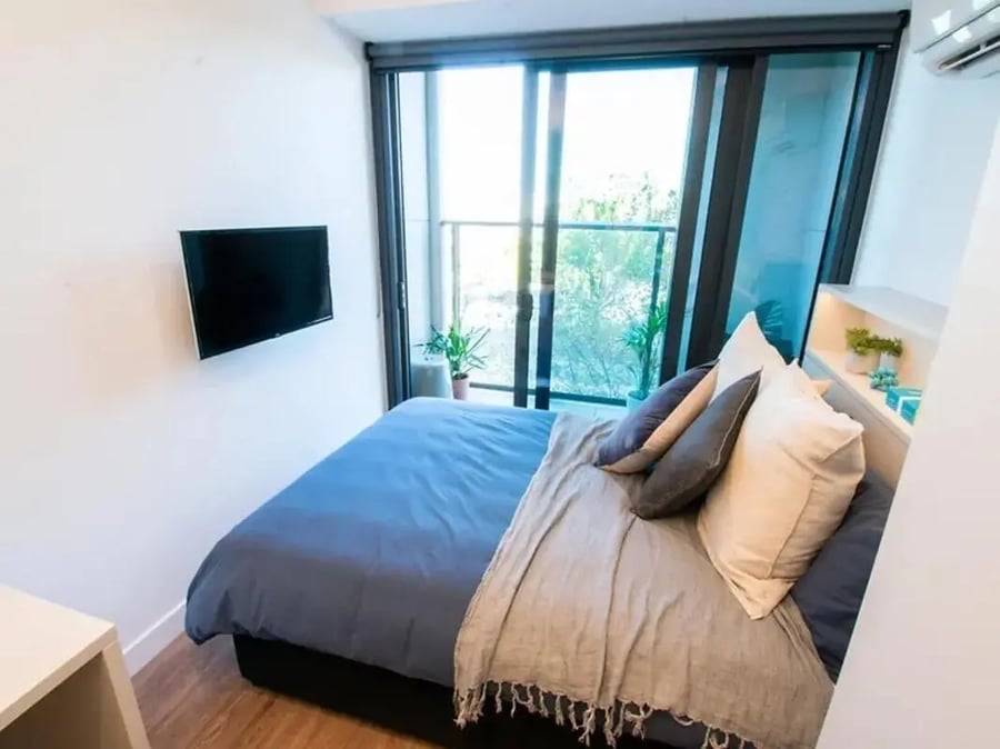 Bed with blue covers mounted TV balcony bedroom at Yugo Berkeley Street in Melbourne Student Accommodation