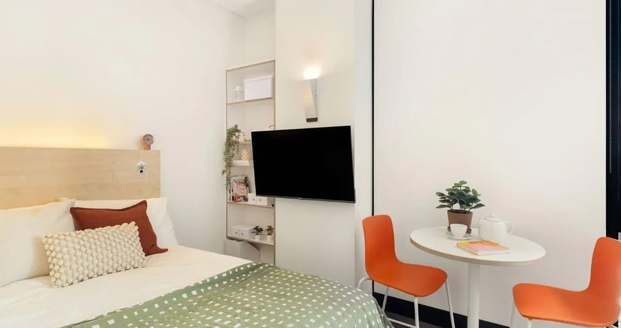 Bed with pillows and duvet table chairs television shelves bedroom at Iglu Chatswood in Sydney Student Accommodation