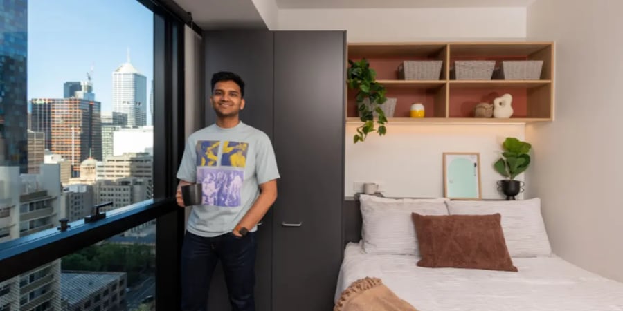 Man holding coffee cup near bed Bedroom at UniLodge Melbourne Central in Melbourne Student Accommodation