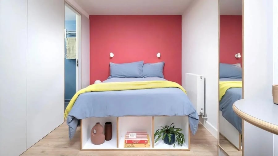 Bed with blue linens yellow throw bookcase bedroom at Scape Kings Cross in London Student Accommodation
