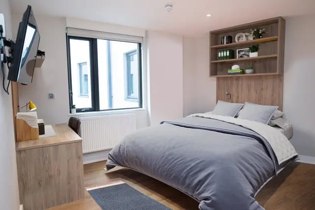 Bed with grey duvet desk shelf TV window bedroom at Canvas Student - Quintana Gate in Exeter Student Accommodation