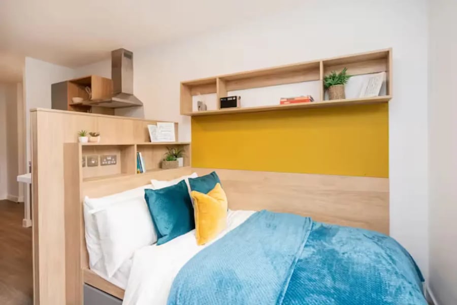 Bed with teal and yellow pillows shelving kitchen area bedroom at Hillfort House in Brighton Student Accommodation