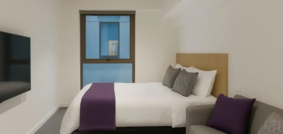 Bed with purple runner grey pillows and sofa bedroom at Unilodge Melbourne City in Melbourne Student Accommodation