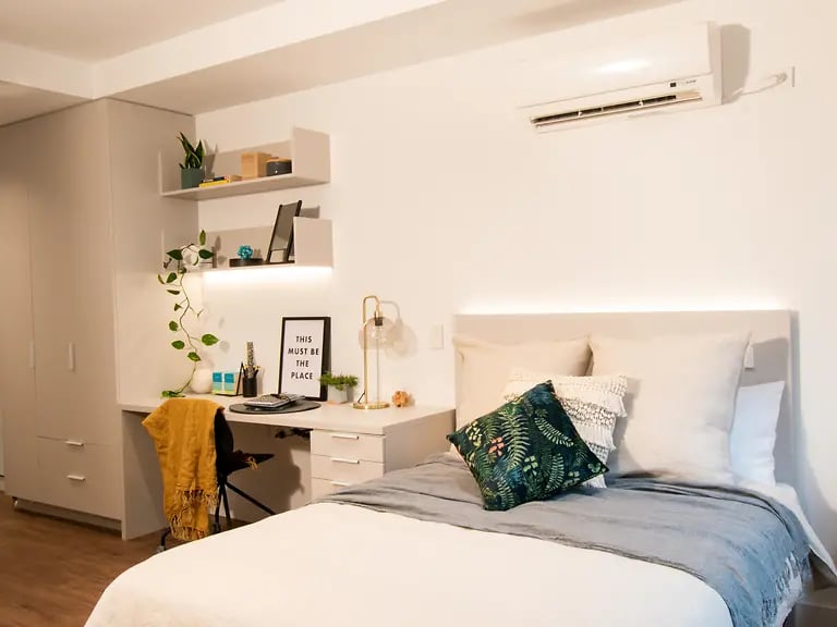 Bed with pillows desk with chair and shelves bedroom at Yugo Berkeley Street in Melbourne Student Accommodation