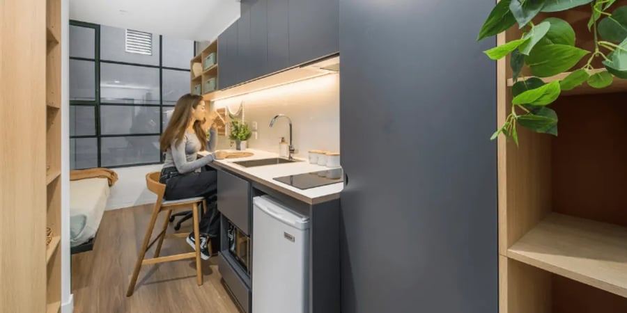 Student sits at kitchen counter near bed kitchen at UniLodge Melbourne Flagstaff in Melbourne Student Accommodation
