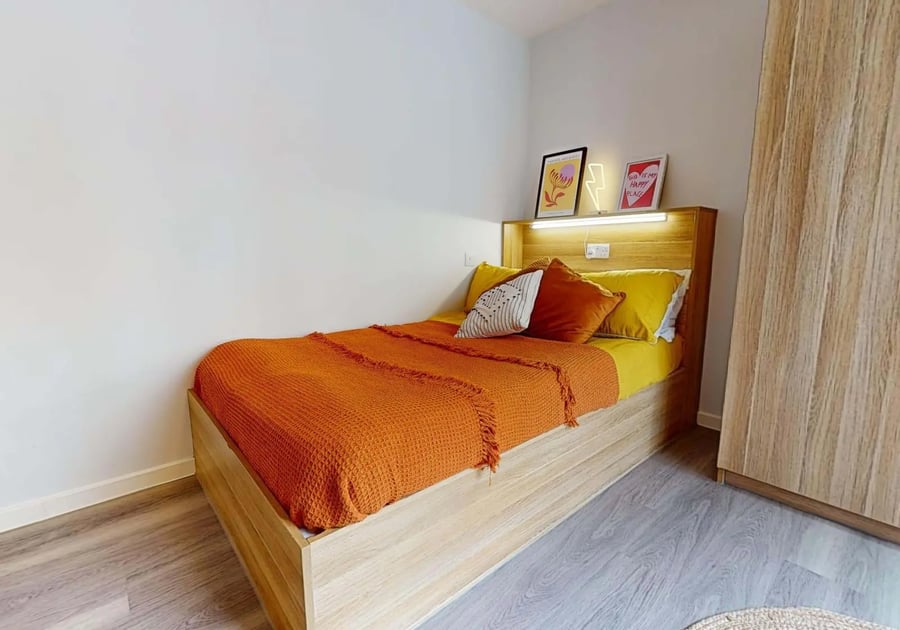 Bed with orange throw pillows and art bedroom at iQ Sterling Court in London Student Accommodation
